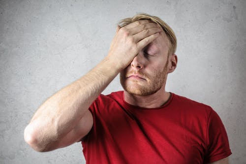frustrated man in red shirt with palm of one hand on forehead